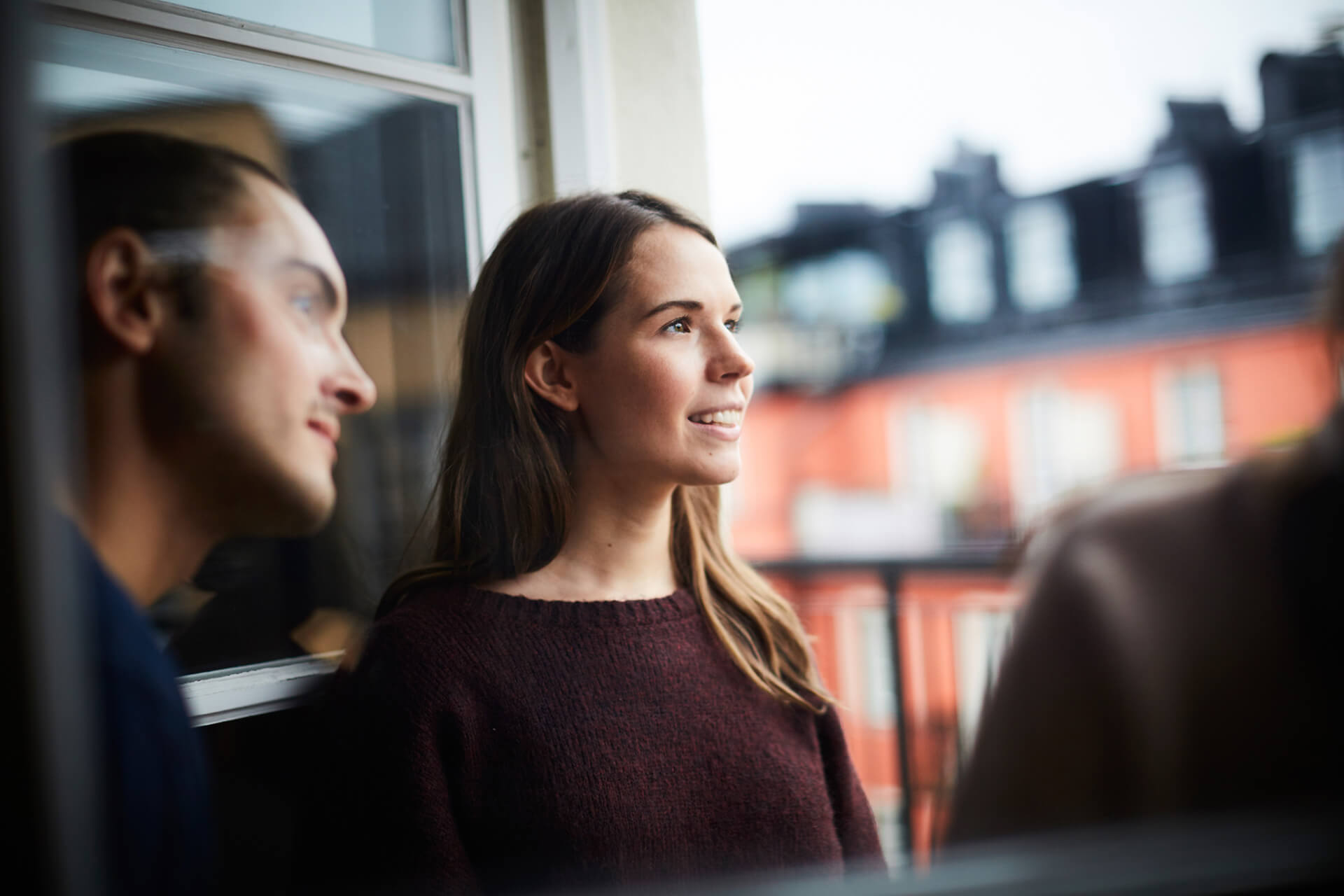 Ungt par tittar ut från balkongen i sin nya lägenhet efter att ha flyttat till en ny kommun, välkomstbrev till nyinflyttade från Lidh Reklam.